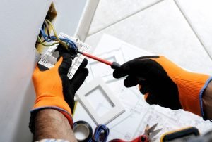 An electrician installs a complex electrical outlet in a wall, showcasing detailed wiring connections. The technician, wearing safety gloves, is carefully attaching wires to the outlet, which highlights the precision and safety measures essential in electrical work. electrical installation, electrician services, wiring installation, safety gloves, professional electrician, Sacramento electrician, Roseville electrical repair, Rocklin home improvement, Folsom electrical services, Auburn electrical upgrades, Citrus Heights wiring experts